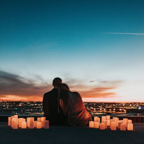 Two people sitting together behind glowing candles overlooking a city at night