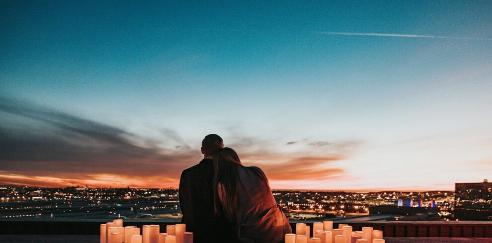Two people sitting together behind glowing candles overlooking a city at night