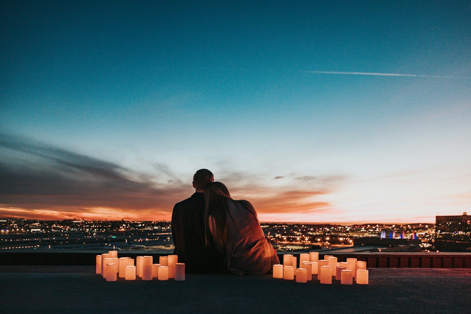 Two people sitting together behind glowing candles overlooking a city at night
